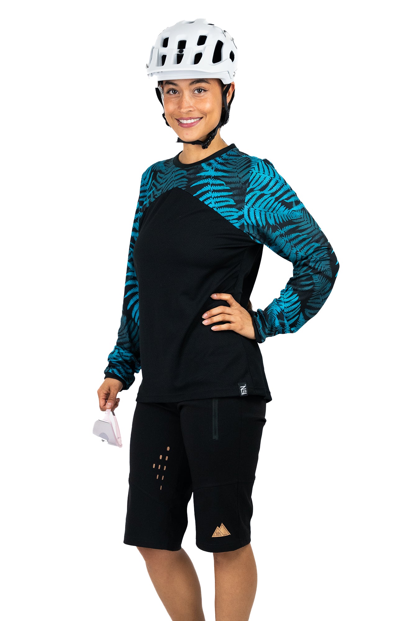 Schwarzes und petrol-grünes Langarm-Mountainbike-Jersey für Frauen mit floralem Farn-Print. Hier dargestellt an einem Modell mit Mountainbikeshort, Helm und Brille.