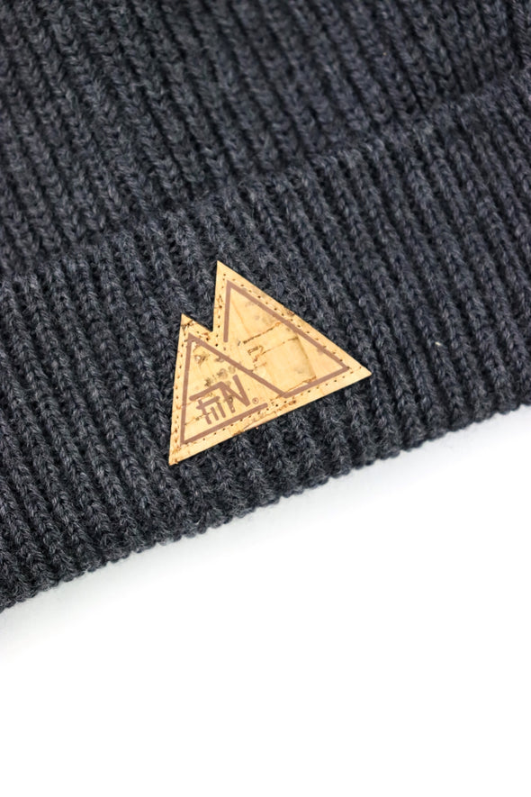 Detail Fiin Logo aus Kork au dem grauen Beanie. Vorne, mittig aufgenäht an der breiten Krempe der Strickmütze. Detail grobe Strickmütze.
