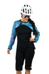 Schwarzes und blau-lila Langarm-Mountainbike-Jersey für Frauen mit floralem Farn-Print. Dargestellt an einem Modell mit Mountainbik Short, Helm und Brille.